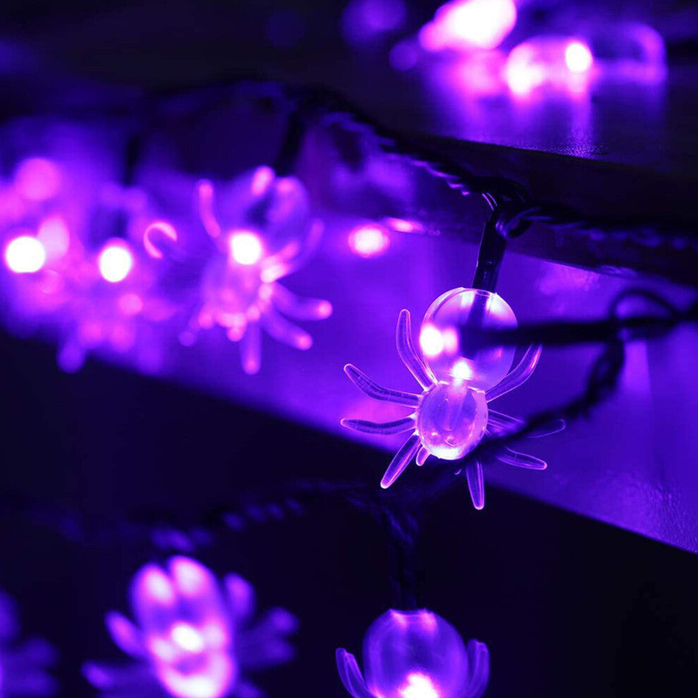 A 20ft string of 40 purple spider-shaped LED lights glowing against an outdoor garden fence at night.