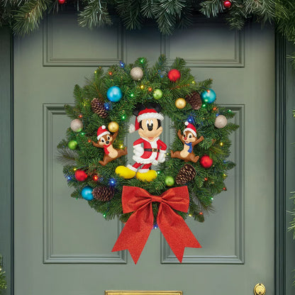 Front view of a 22-inch lush green Christmas wreath featuring Mickey Mouse and friends ornaments illuminated by warm battery-operated LED lights hanging on a wooden door.