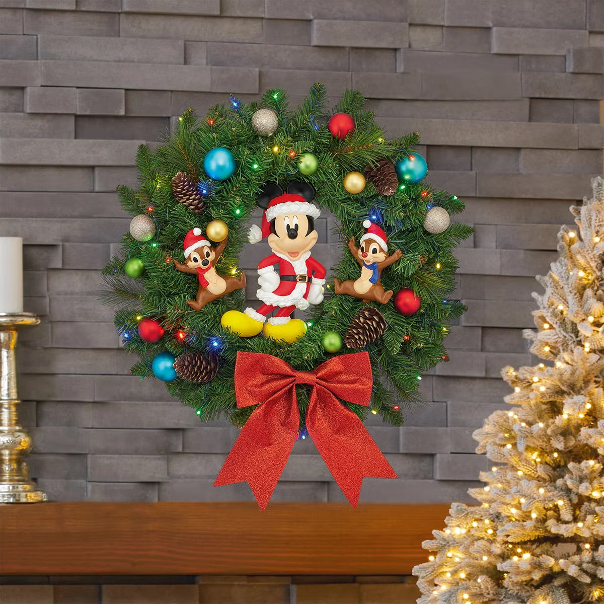 Front view of a 22-inch lush green Christmas wreath featuring Mickey Mouse and friends ornaments illuminated by warm battery-operated LED lights hanging on a wooden door.