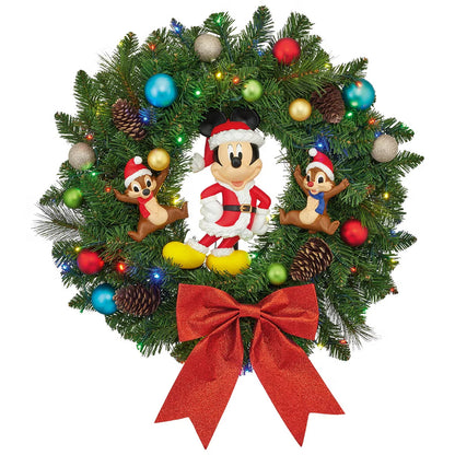 Front view of a 22-inch lush green Christmas wreath featuring Mickey Mouse and friends ornaments illuminated by warm battery-operated LED lights hanging on a wooden door.