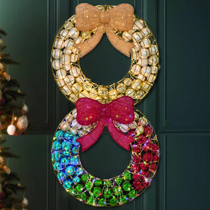 Frontal view of a 24-inch red indoor holiday wreath made of glossy and matte ornaments glowing with warm white LED lights over a dark brick mantelpiece.
