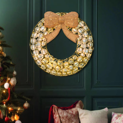 Frontal view of a 24-inch red indoor holiday wreath made of glossy and matte ornaments glowing with warm white LED lights over a dark brick mantelpiece.