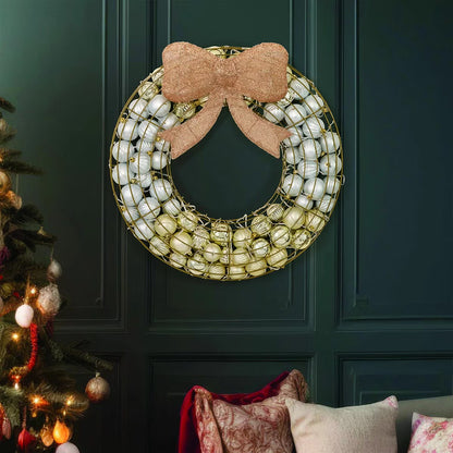 Frontal view of a 24-inch red indoor holiday wreath made of glossy and matte ornaments glowing with warm white LED lights over a dark brick mantelpiece.