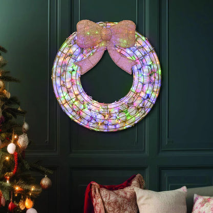 Frontal view of a 24-inch red indoor holiday wreath made of glossy and matte ornaments glowing with warm white LED lights over a dark brick mantelpiece.