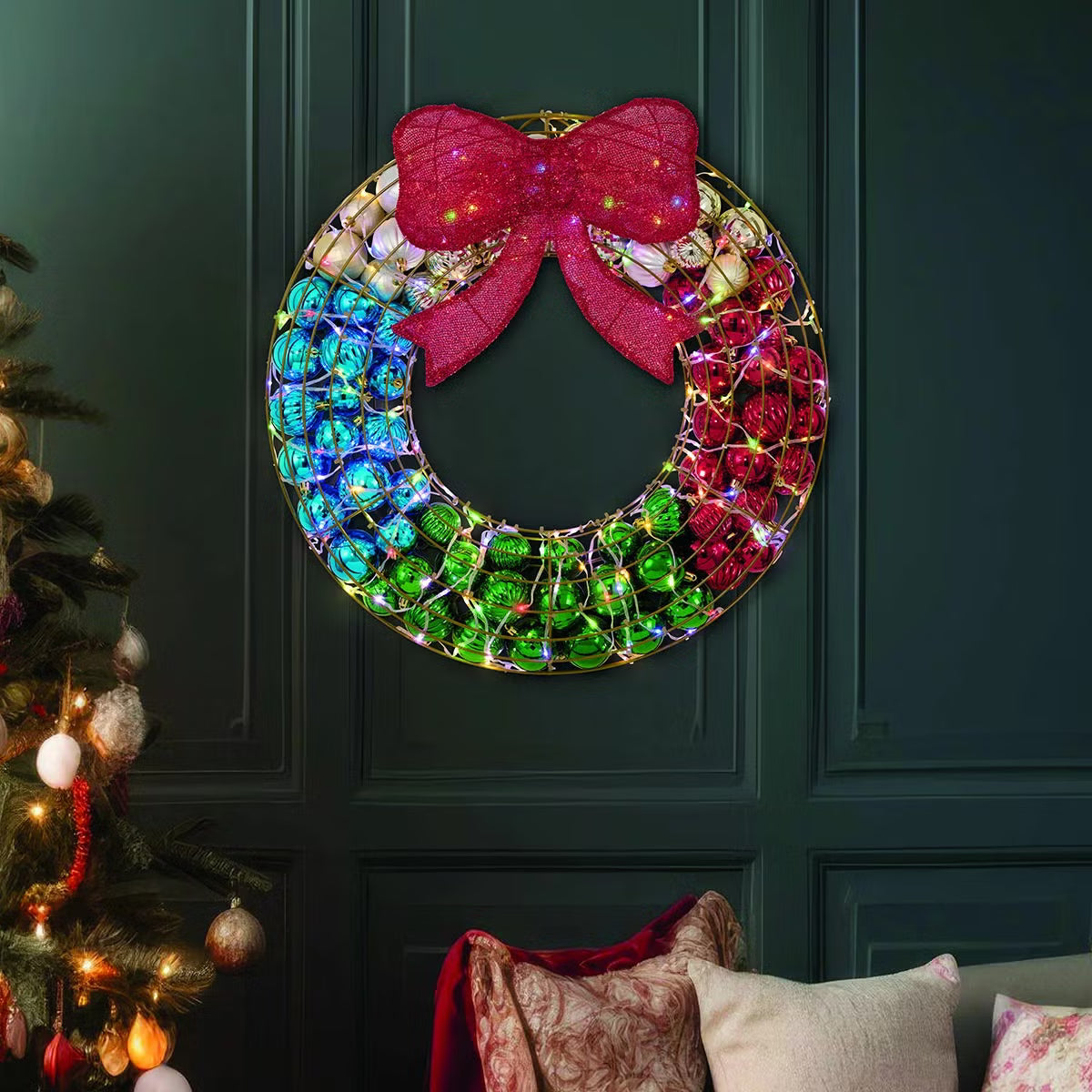 Frontal view of a 24-inch red indoor holiday wreath made of glossy and matte ornaments glowing with warm white LED lights over a dark brick mantelpiece.