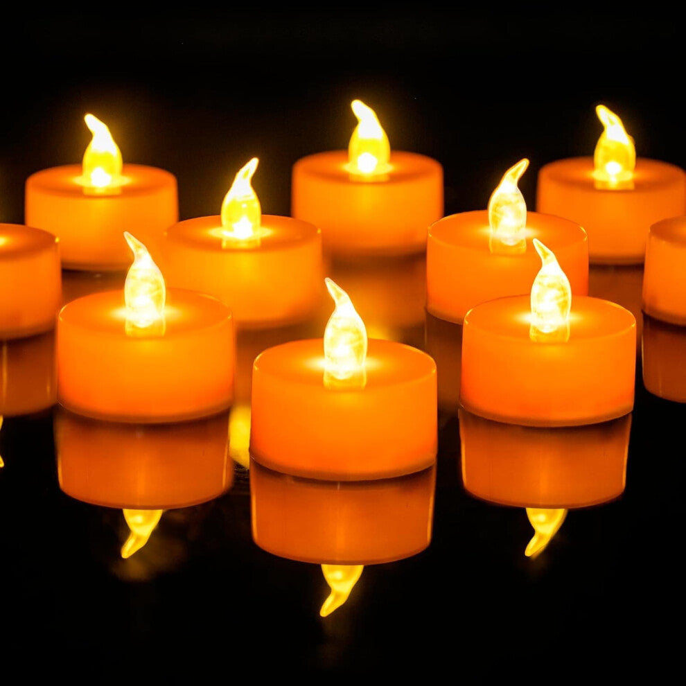 A 24-pack of orange LED flameless flickering tea light candles glowing warmly on a dark table decorated for Halloween.
