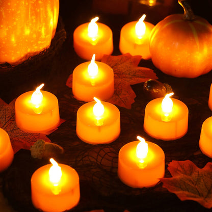 A 24-pack of orange LED flameless flickering tea light candles glowing warmly on a dark table decorated for Halloween.