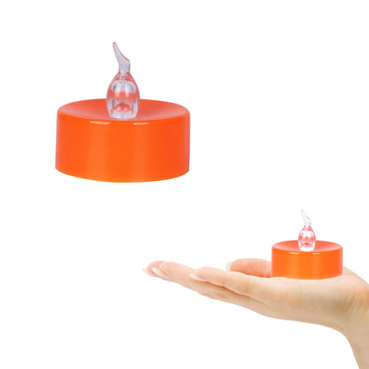 A 24-pack of orange LED flameless flickering tea light candles glowing warmly on a dark table decorated for Halloween.