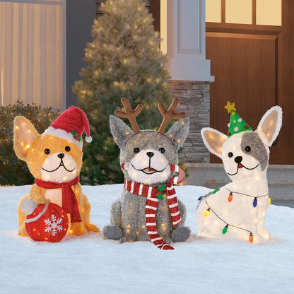 Three illuminated outdoor LED Christmas dog figures standing on a green lawn wearing festive scarves and headbands at twilight.