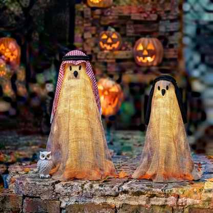 A pair of tall outdoor Halloween spooky ghost decorations illuminated by remote-controlled string lights on a dark lawn during evening hours.