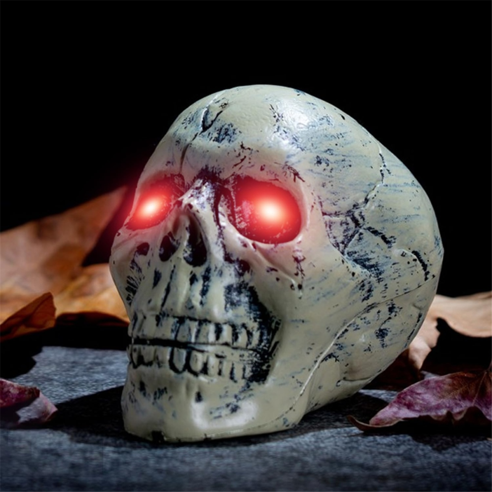 A pair of glowing red LED skeleton eyes mounted inside a dark Halloween prop skull outdoors at night.