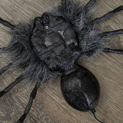 Black faux-fur animatronic spider with glowing red eyes hanging from a suspended string against a dark background.
