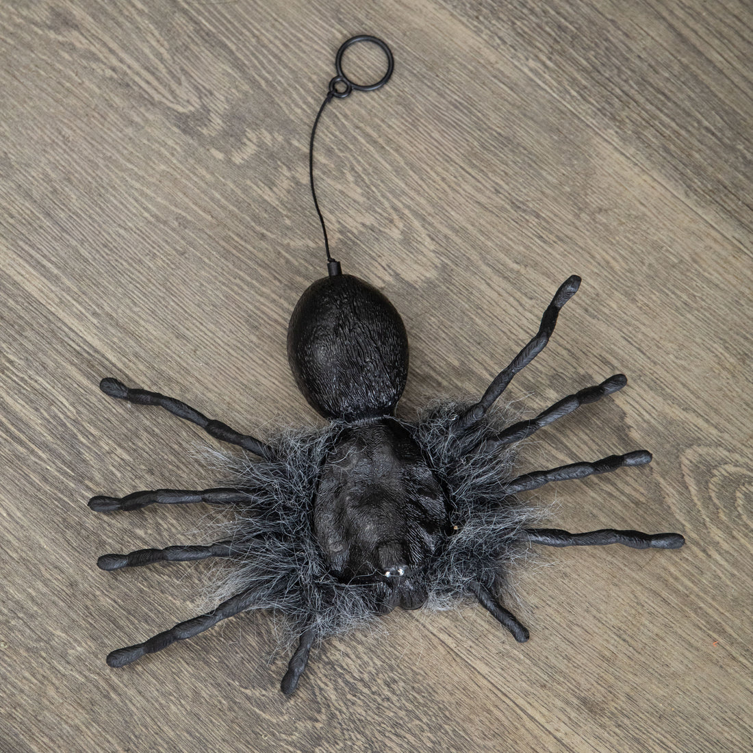 Black faux-fur animatronic spider with glowing red eyes hanging from a suspended string against a dark background.