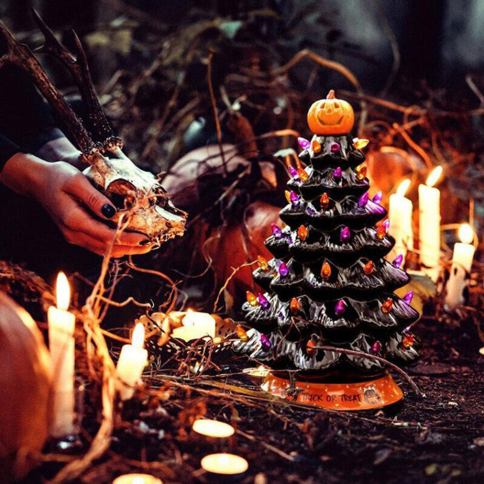 A 30cm black tabletop Halloween tree decorated with glowing pumpkin LED lights and warm white flashing beads sitting on a festive wooden surface.