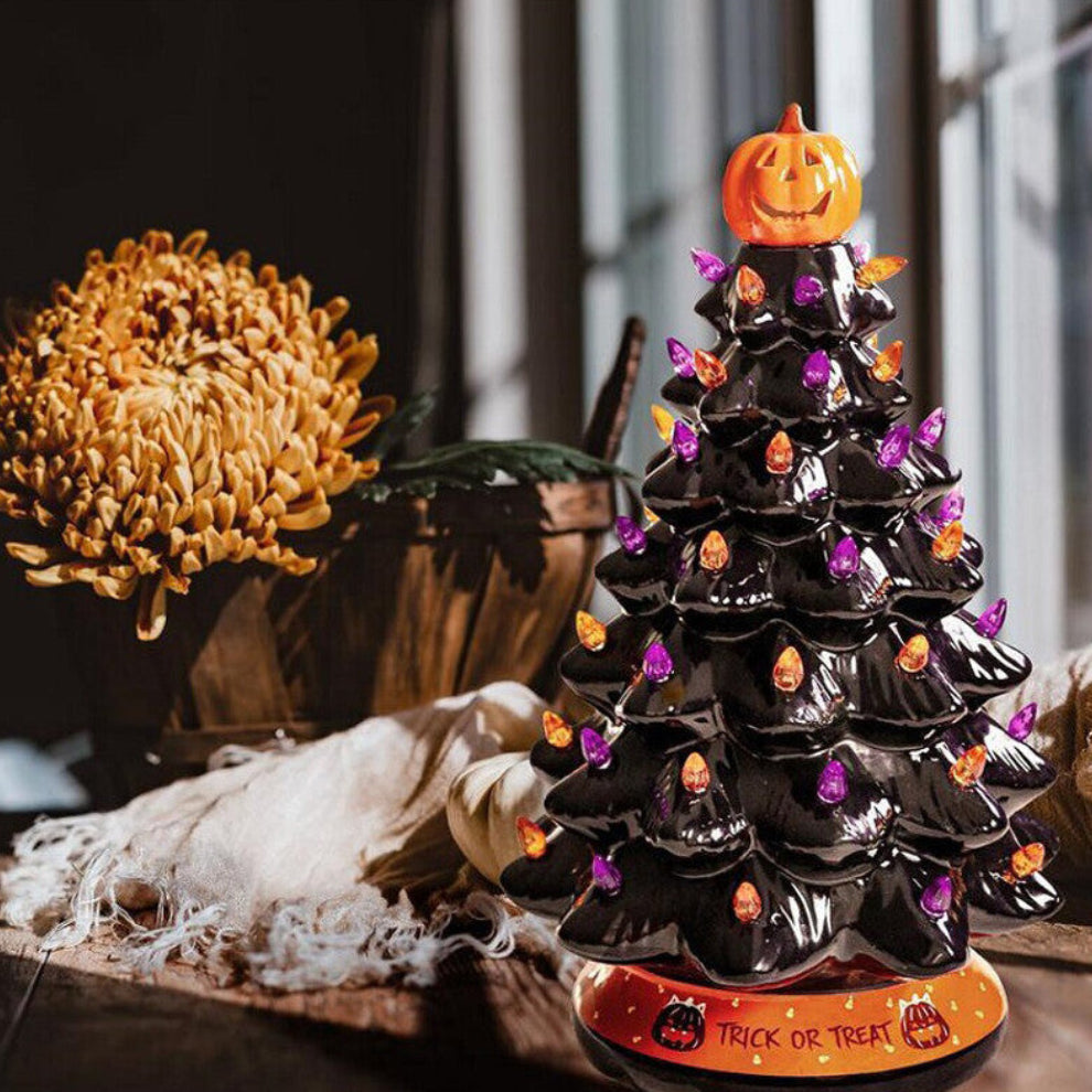 A 30cm black tabletop Halloween tree decorated with glowing pumpkin LED lights and warm white flashing beads sitting on a festive wooden surface.