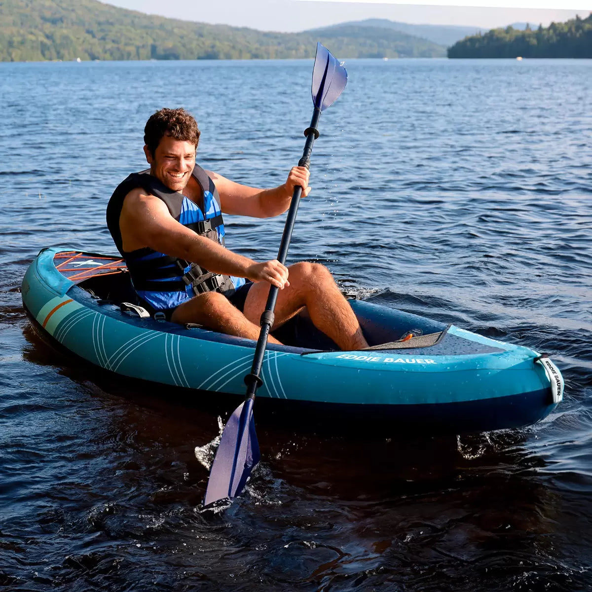 Eddie Bauer 10ft inflatable sit-in kayak with paddle on a calm blue lake.