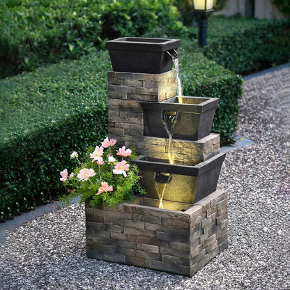 A 34.5-inch tiered brick-effect fountain glowing with warm LED lights on a stone patio, surrounded by green foliage at dusk