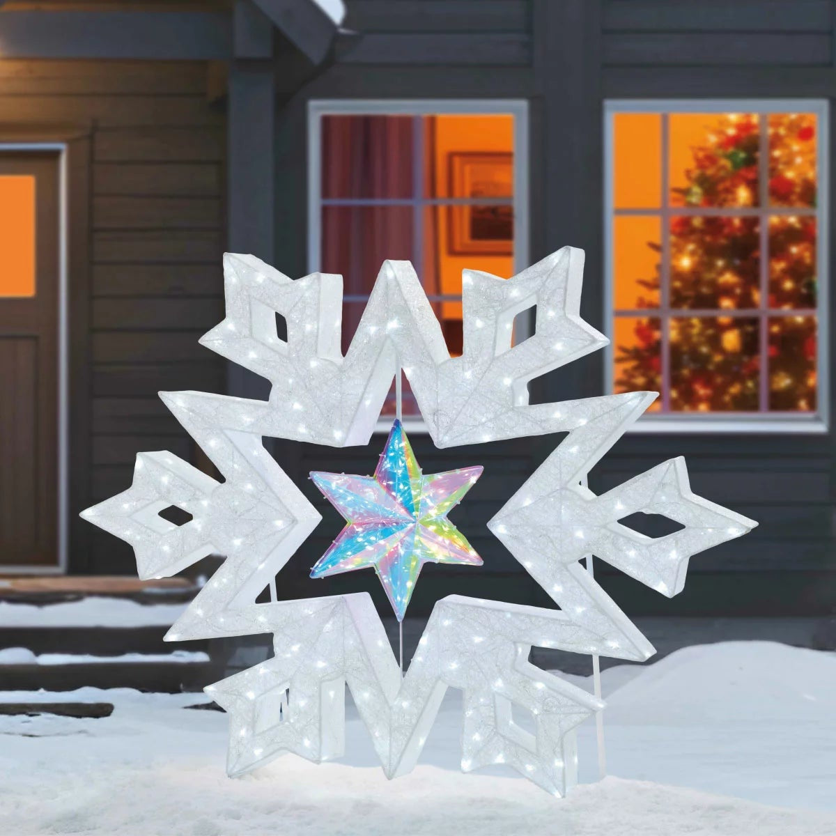 A 48-inch illuminated white LED snowflake holiday light with a center rotating prismatic star glowing brightly on a dark green outdoor lawn at night.