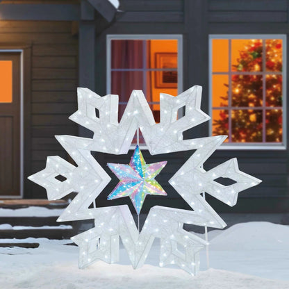 A 48-inch illuminated white LED snowflake holiday light with a center rotating prismatic star glowing brightly on a dark green outdoor lawn at night.