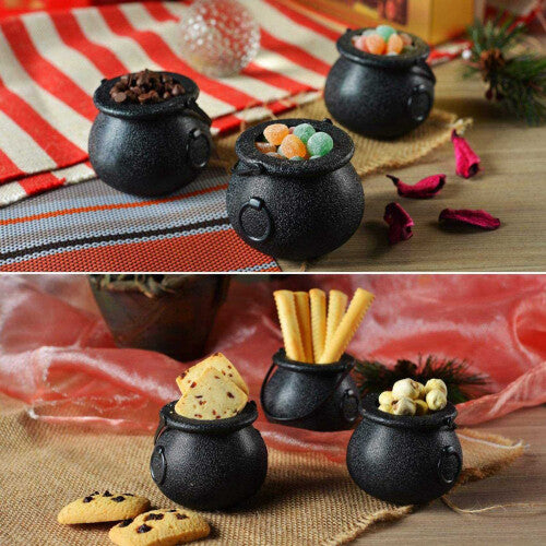 A group of mini black plastic witch candy cauldrons with curved handles arranged on a table filled with Halloween treats.
