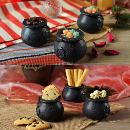A group of mini black plastic witch candy cauldrons with curved handles arranged on a table filled with Halloween treats.