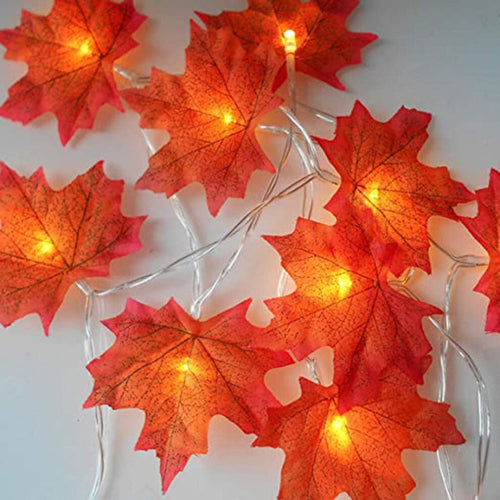A 4m 40LED plug-in fall maple leaves string light glowing warmly on a rustic wooden mantelpiece decorated for Halloween and Thanksgiving.