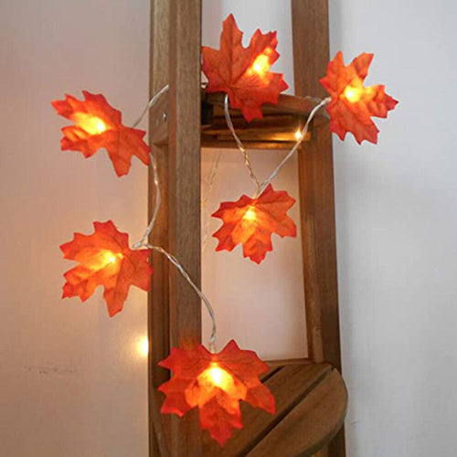 A 4m 40LED plug-in fall maple leaves string light glowing warmly on a rustic wooden mantelpiece decorated for Halloween and Thanksgiving.