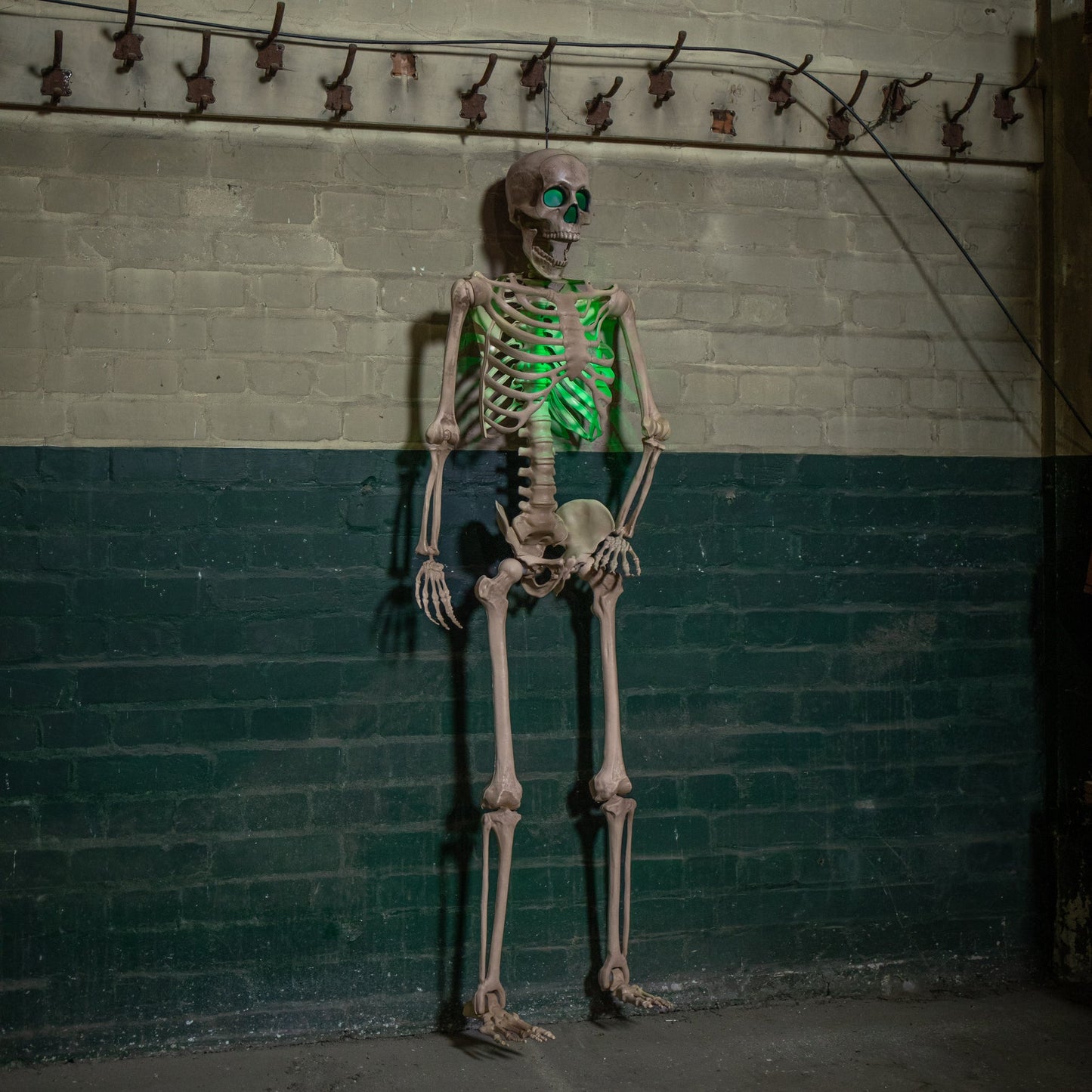 Life sized 5ft poseable Halloween skeleton prop with glowing green LED eyes and ribs standing on a covered dark wooden porch