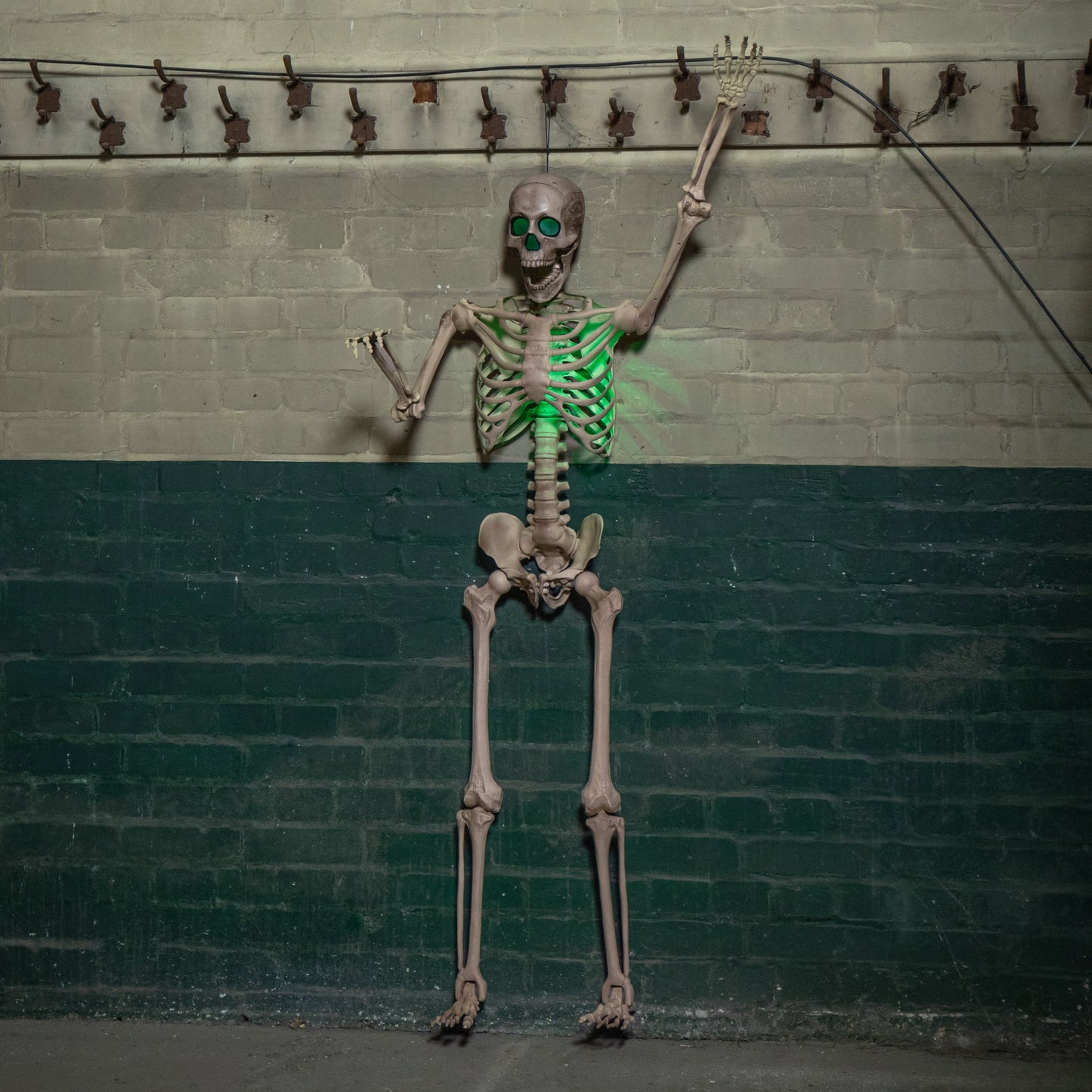 Life sized 5ft poseable Halloween skeleton prop with glowing green LED eyes and ribs standing on a covered dark wooden porch