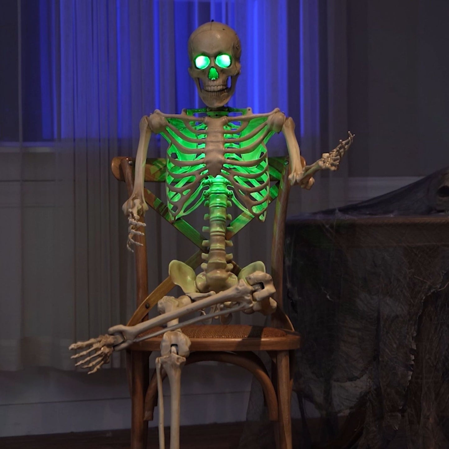Life sized 5ft poseable Halloween skeleton prop with glowing green LED eyes and ribs standing on a covered dark wooden porch