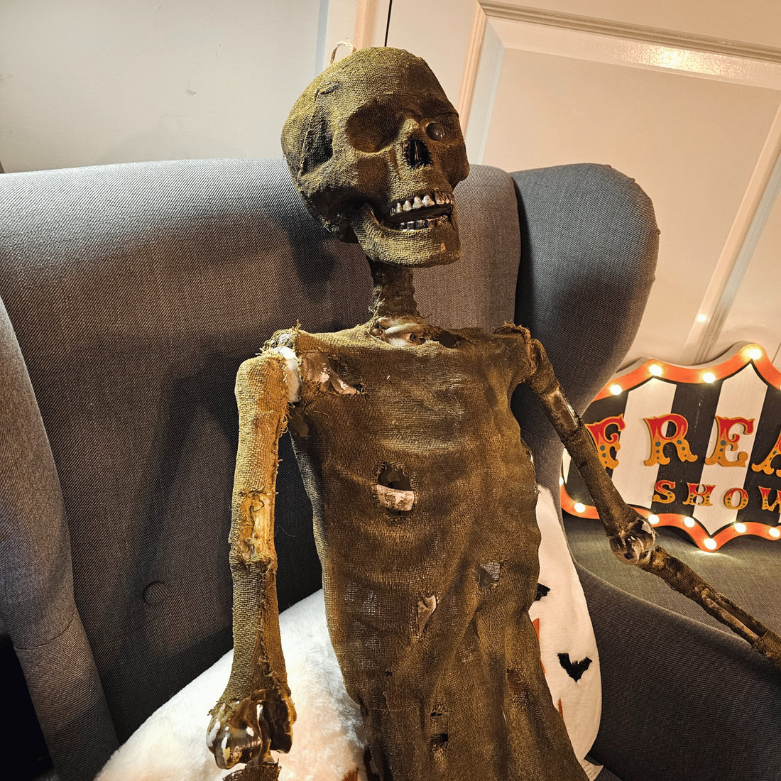 Front view of a 5ft tall brown mummified skeleton prop with posable joints and a distressed finish hanging against a dark background.