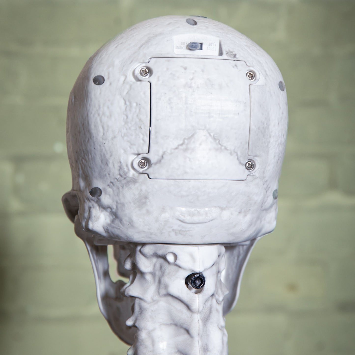 Front view of a grey 5ft full body Halloween skeleton with glowing red LED eyes standing upright on a black metal base on a porch.