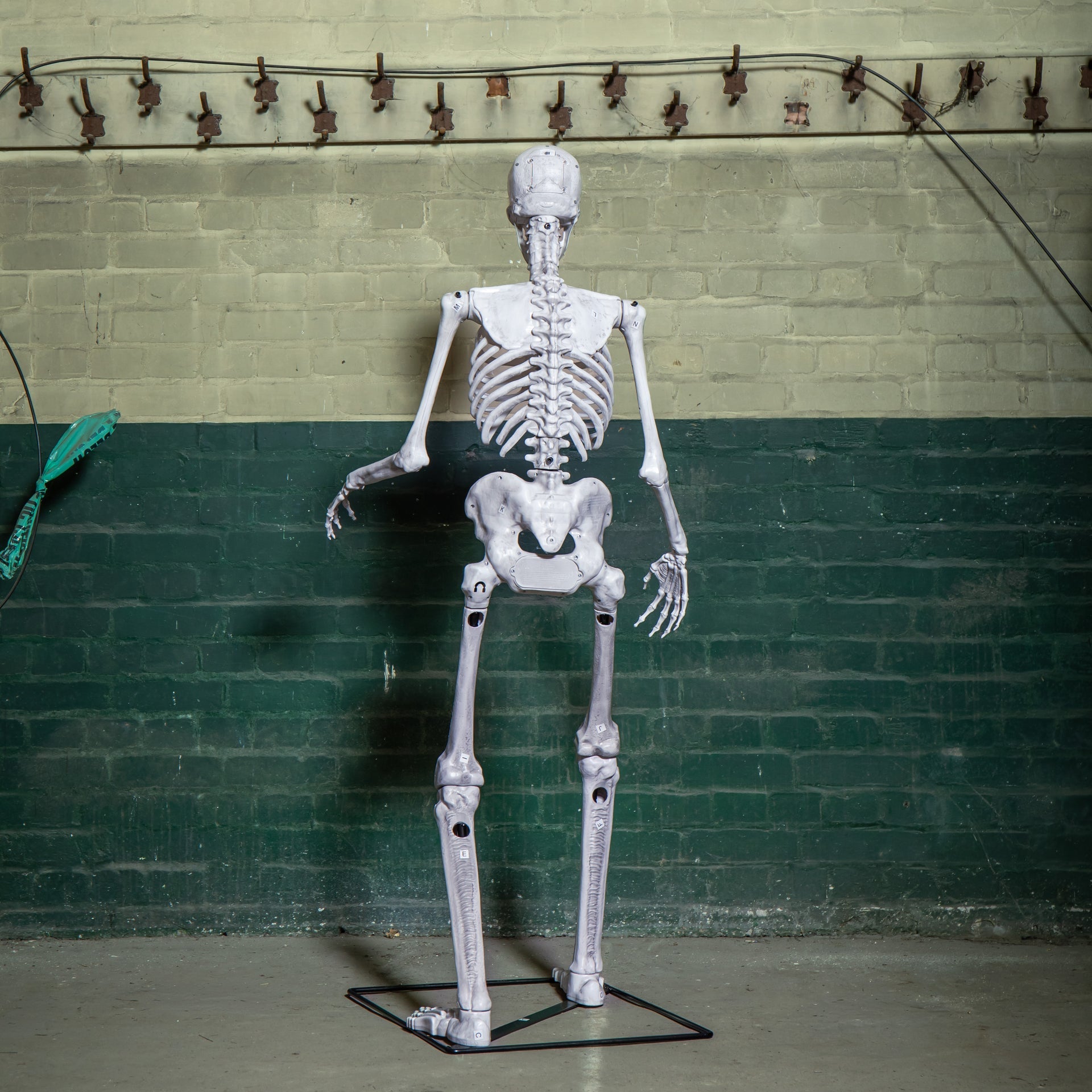 Front view of a grey 5ft full body Halloween skeleton with glowing red LED eyes standing upright on a black metal base on a porch.