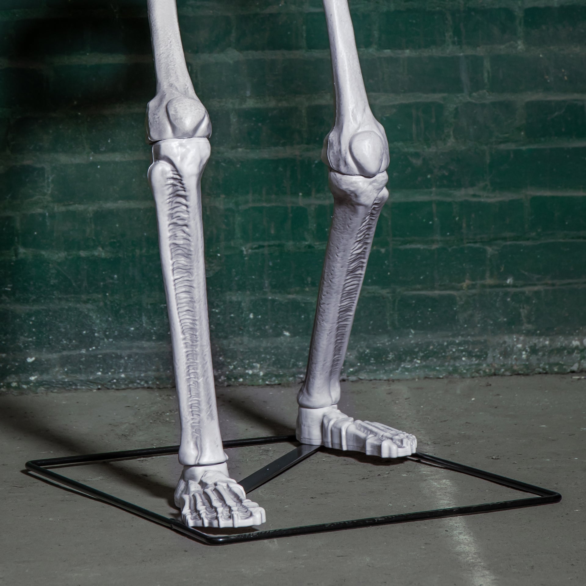 Front view of a grey 5ft full body Halloween skeleton with glowing red LED eyes standing upright on a black metal base on a porch.