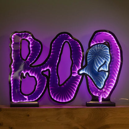 Samuel Alexander 60cm illuminated BOO infinity mirror sign with glowing pink and white LEDs mounted on a wooden base displayed on a fireplace mantel.