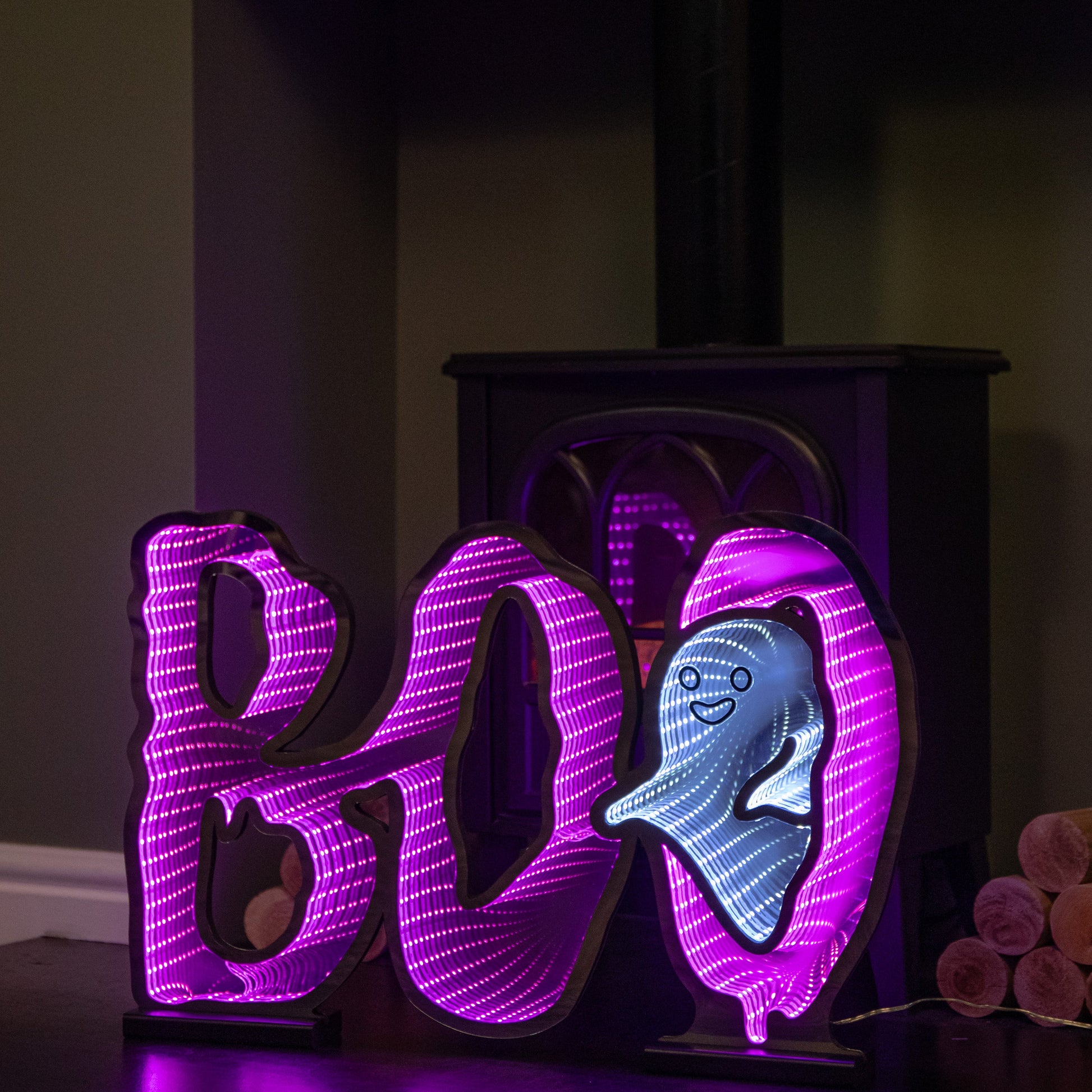 Samuel Alexander 60cm illuminated BOO infinity mirror sign with glowing pink and white LEDs mounted on a wooden base displayed on a fireplace mantel.