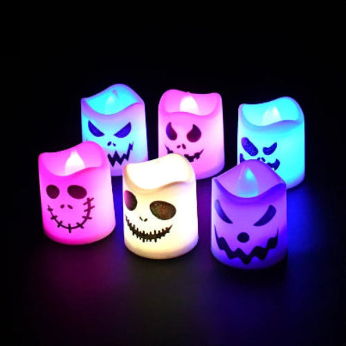 A set of 6 multicolor LED Halloween ghost and pumpkin tealight candles glowing warmly on a dark table setup for a party.
