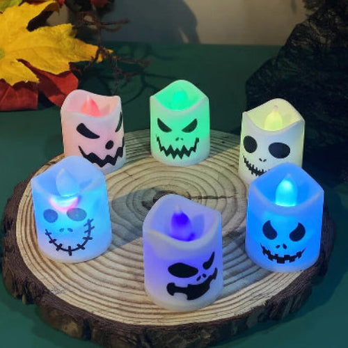 A set of 6 multicolor LED Halloween ghost and pumpkin tealight candles glowing warmly on a dark table setup for a party.