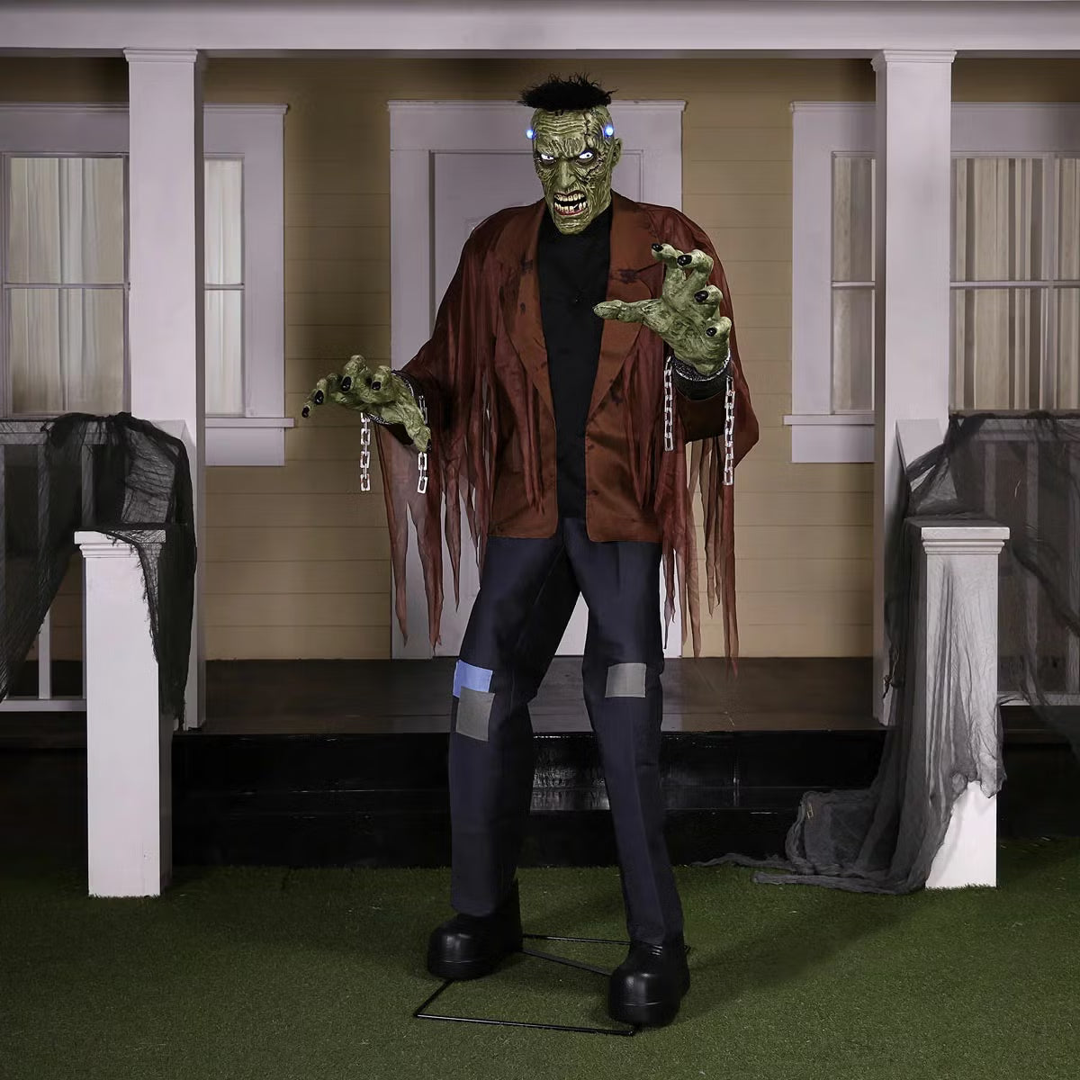 Front view of a 7.5ft tall animated Frankenstein monster prop with glowing blue LCD eyes, rugged green skin, torn jacket, and flickering head electrodes standing outdoors.