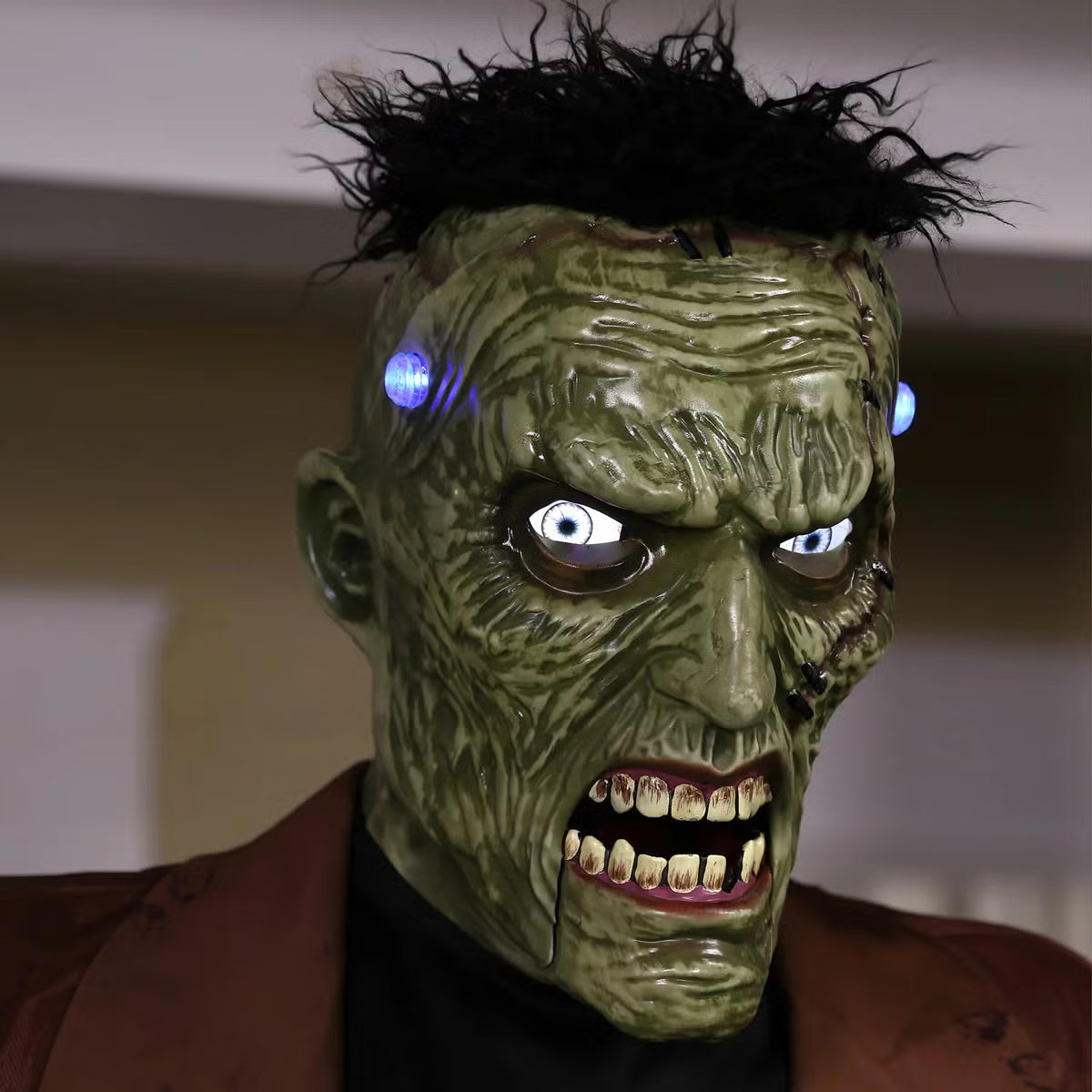 Front view of a 7.5ft tall animated Frankenstein monster prop with glowing blue LCD eyes, rugged green skin, torn jacket, and flickering head electrodes standing outdoors.