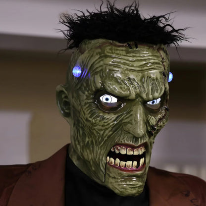 Front view of a 7.5ft tall animated Frankenstein monster prop with glowing blue LCD eyes, rugged green skin, torn jacket, and flickering head electrodes standing outdoors.