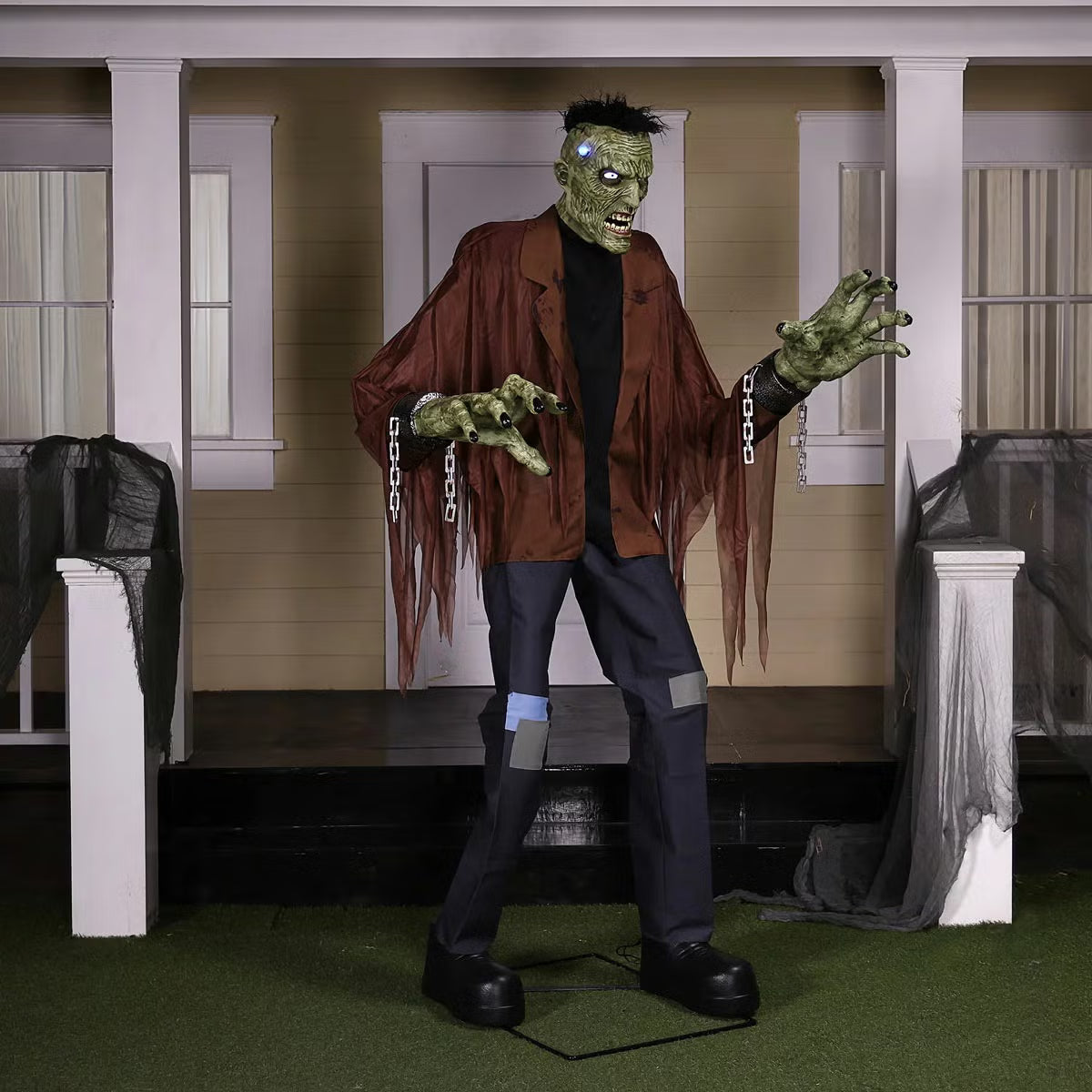Front view of a 7.5ft tall animated Frankenstein monster prop with glowing blue LCD eyes, rugged green skin, torn jacket, and flickering head electrodes standing outdoors.