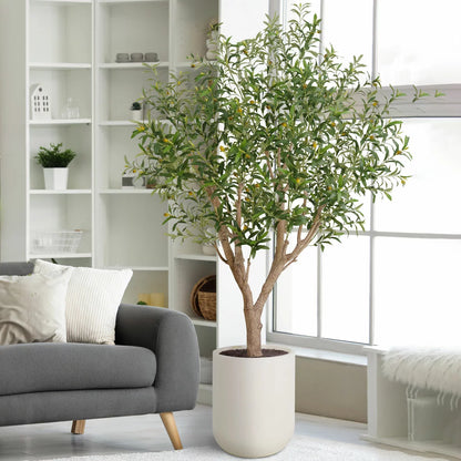 An 8ft artificial olive tree with realistic silvery-green leaves and a hand-painted trunk, potted in a modern white planter and positioned in a sunlit, minimalist living room.