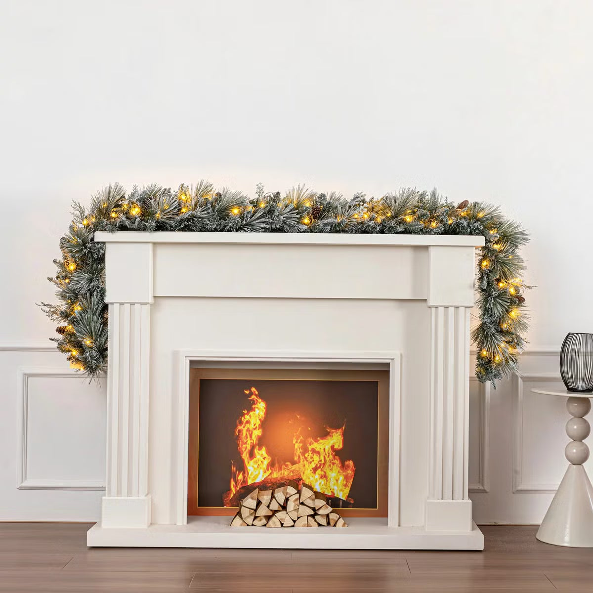 Close-up angle of a 9ft pre-lit flocked garland adorned with 150 glowing micro LED lights, pinecones, and frosted green needles draped across a rustic wooden mantel.