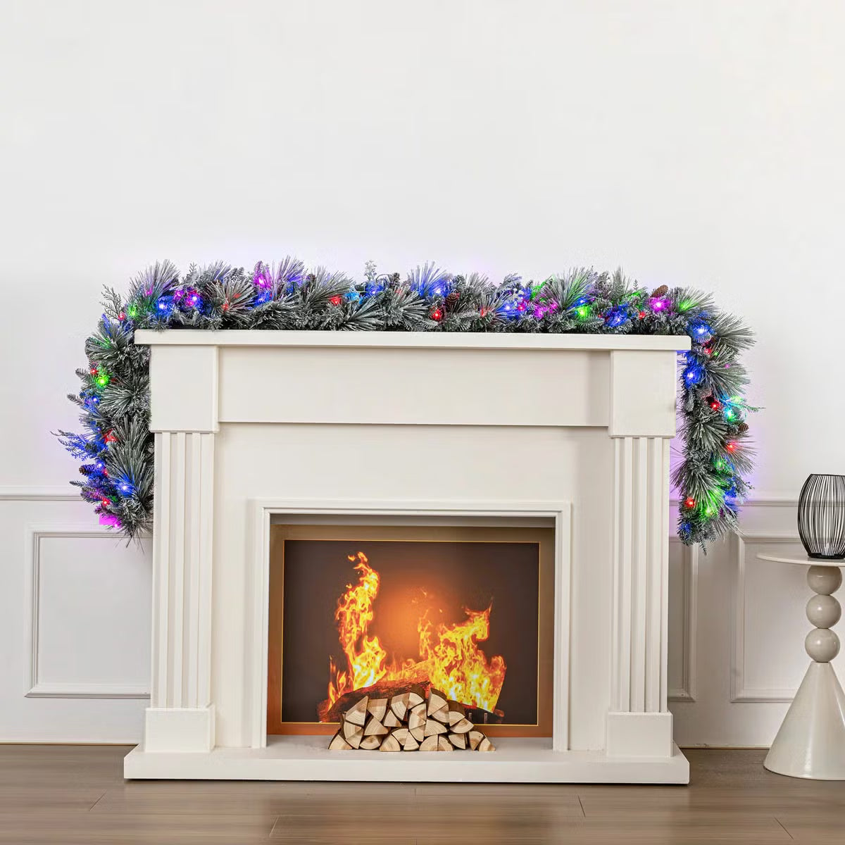 Close-up angle of a 9ft pre-lit flocked garland adorned with 150 glowing micro LED lights, pinecones, and frosted green needles draped across a rustic wooden mantel.