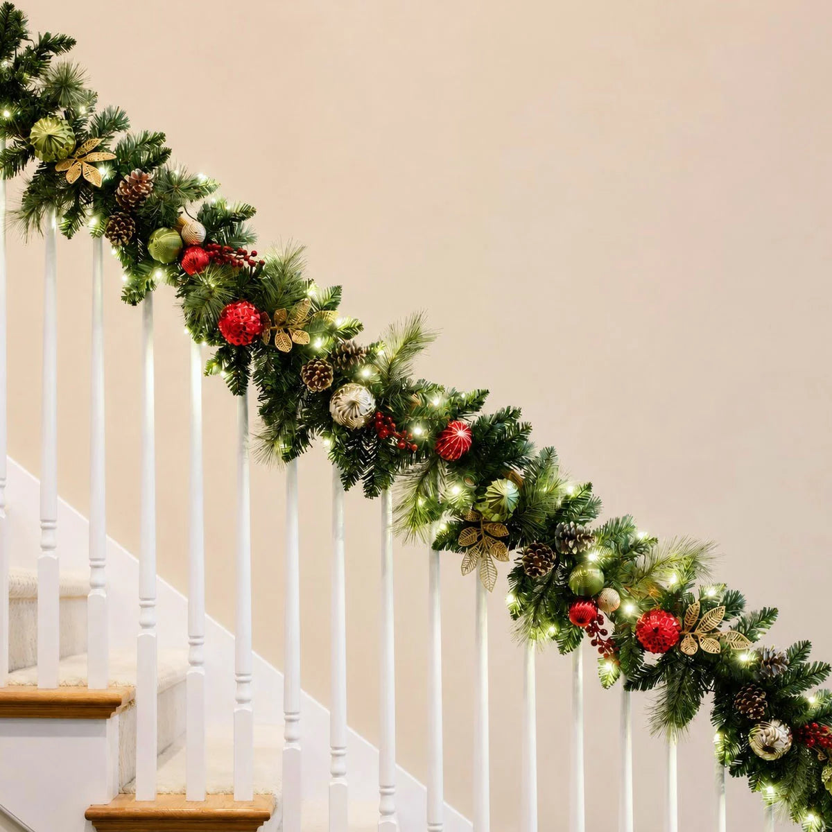 Close-up of a 9ft pre-lit artificial Christmas garland featuring 90 warm white glowing LED lights, realistic pine branches, pinecones, and red festive ornaments draped indoors.