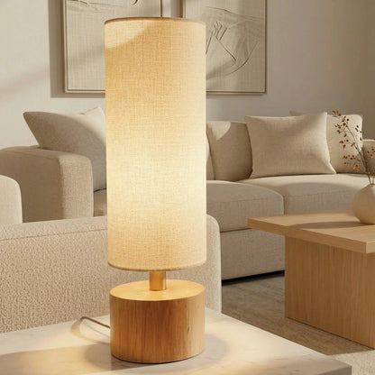 Natural rubberwood base of the Adesso Brayden table lamp with a beige fabric shade on a wooden side table.