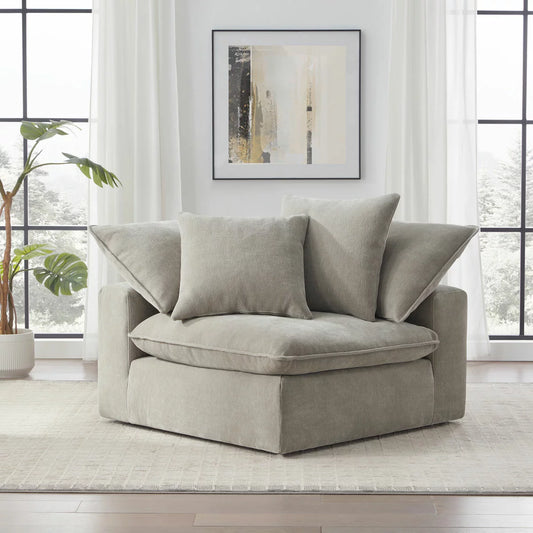 Side angle view of the Aiden & Ivy Sereen modular corner chair upholstered in textured beige fabric with two matching feather pillows resting against the backrest on a clean wooden floor.