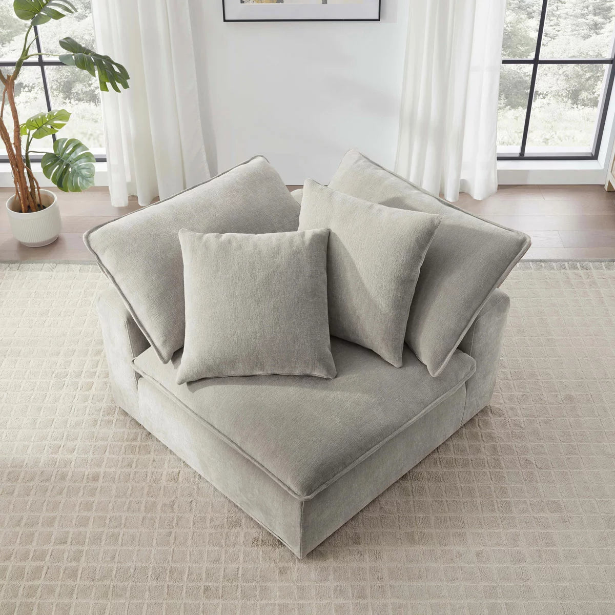 Side angle view of the Aiden & Ivy Sereen modular corner chair upholstered in textured beige fabric with two matching feather pillows resting against the backrest on a clean wooden floor.