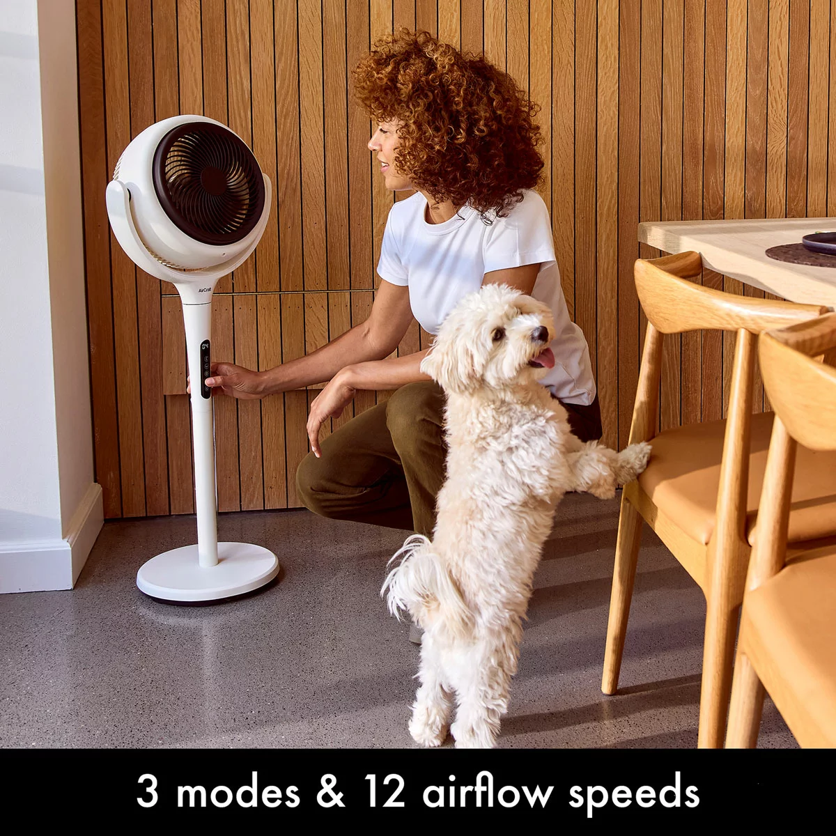 Convertible stone white AirCraft LUME 2-in-1 air circulator fan with illuminated rear backlight standing on a wooden floor beside a lounge sofa.